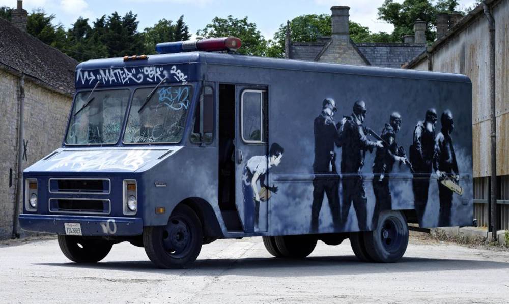 SWAT-køretøjets ene side forestiller svært bevæbnede Special Forces-agenter, der bliver holdt for nar af en lille dreng. Banksy Graffiti Van