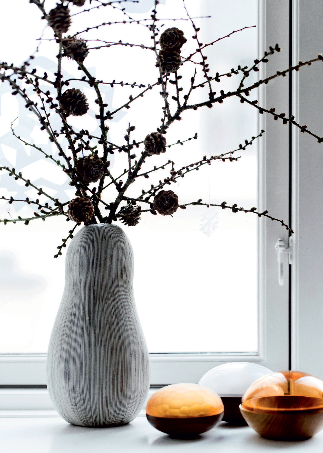 En nærmest grafisk smuk buket grene med kogler spreder julestemning i vindueskarmen.