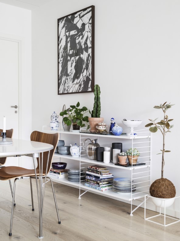 Åbne hylder ved spisepladsen skaber stemning og giver plads til bøger og fint arvet porcelæn fra Katharinas elskede farmor. Reoler fra String fyldt med vintage porcelæn og Lyngbyvaser. Kæmpe sukkulent fra Planteplaneter i plantestand på gulvet fra Menu. Værk på væggen fra Playtype.