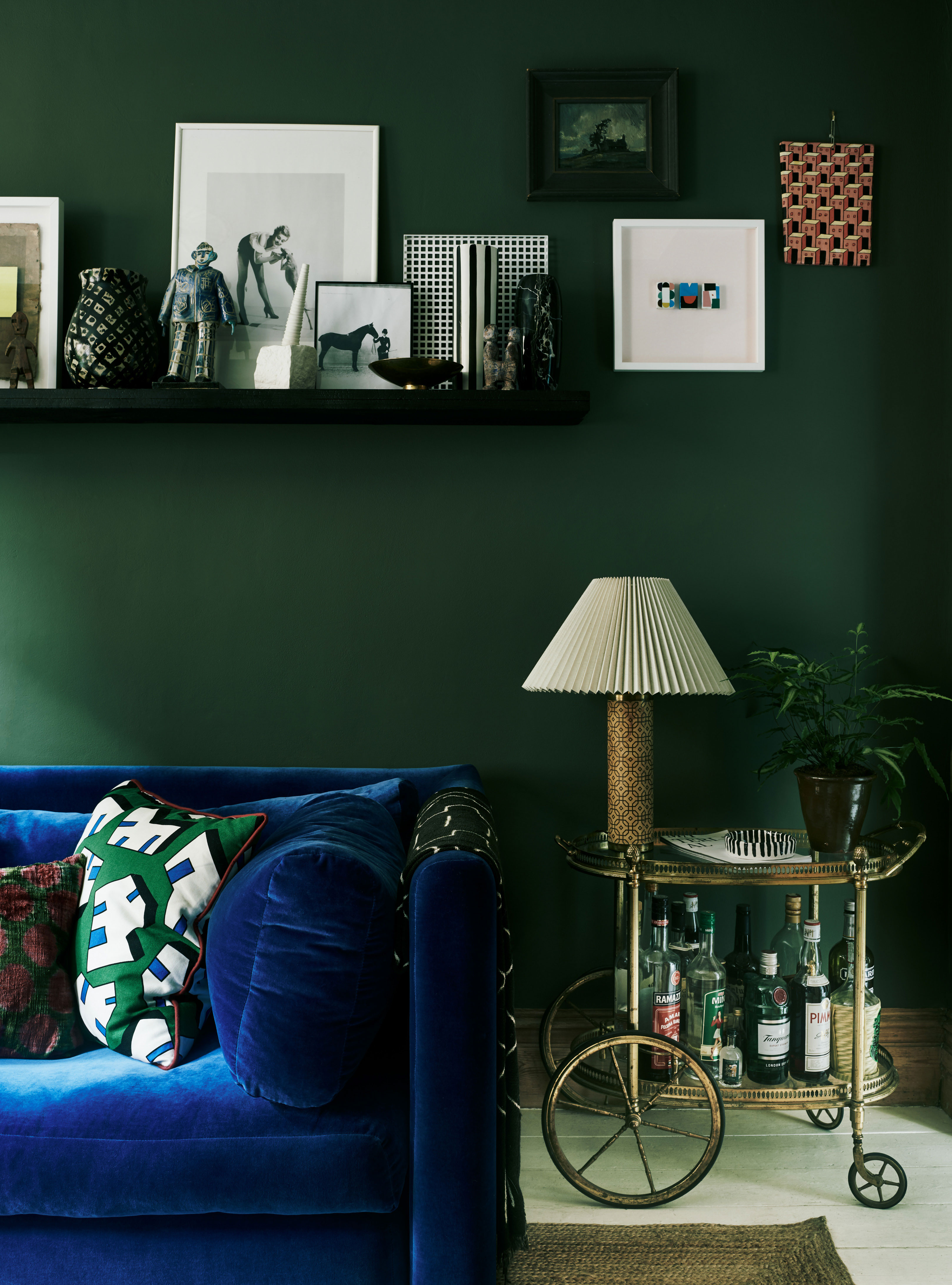 Til den grønne væg i stuen har Laura valgt en blå veloursofa fra Hay. Ovenover på hylden har hun udstillet en blanding af kunst og kuriosa. Barvognen er et vintagefund – for lignende prøv Roxy Klassik eller lauritz.com