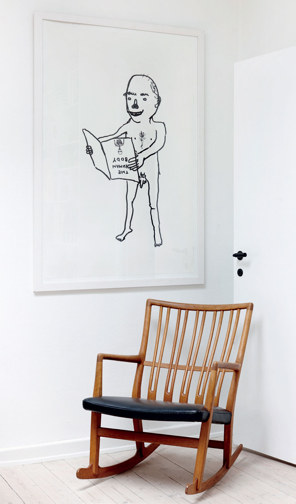 Et lyst og roligt læsehjørne med arvet stol og et billede af David Shrigley.