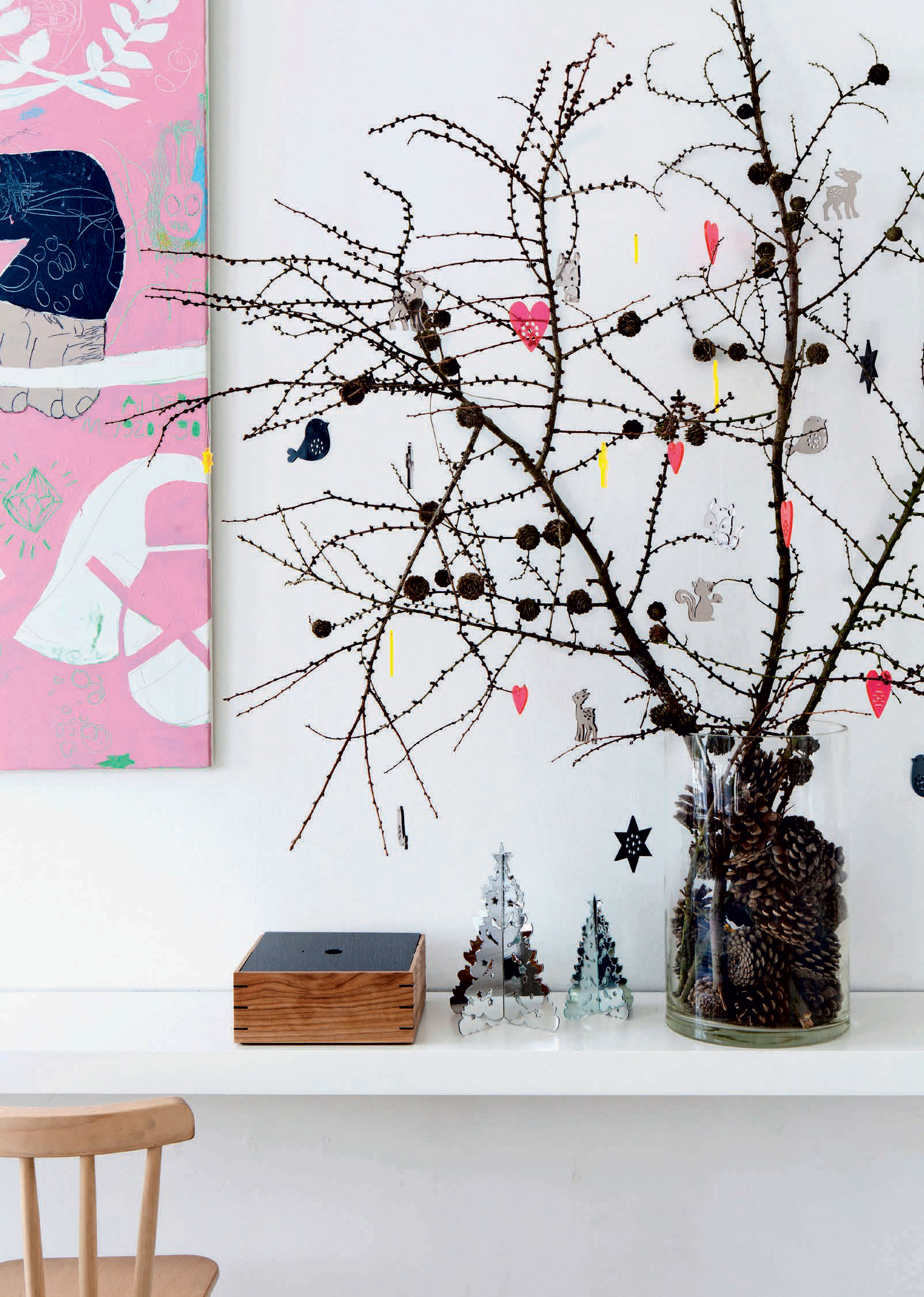 En glasvase med kogler og nogle grene fra skoven danner en smuk base for Sidsels farverige julepynt i plexiglas.